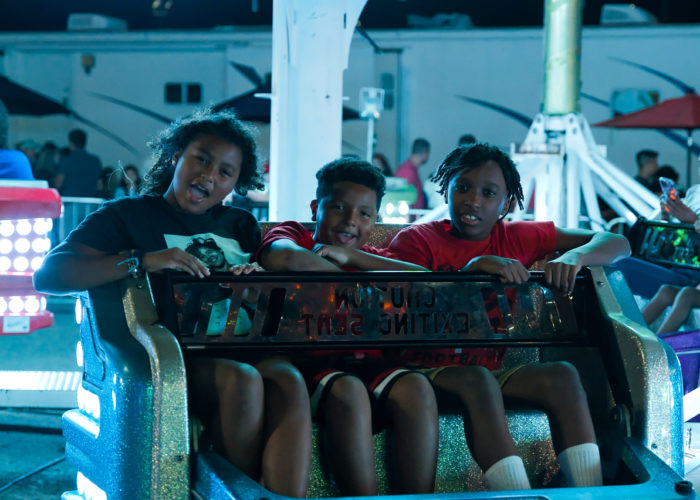 Three young people sit on carnival ride. Credit: Ahmod Goins